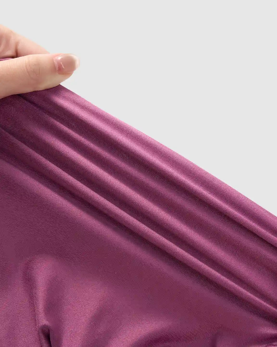 Hand stretching the soft, supportive plum-colored fabric of Bump Society's slim-fitting maternity joggers.