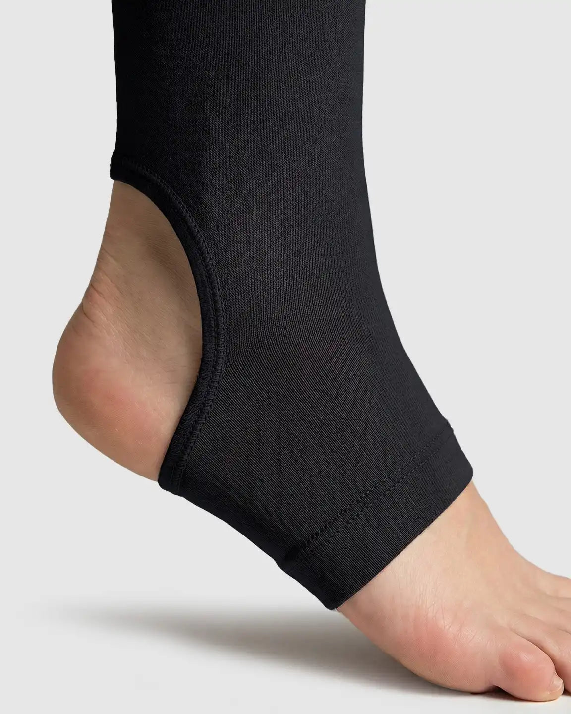 Close-up of a foot in black fleece-lined maternity stirrup leggings, showing the ankle and heel.