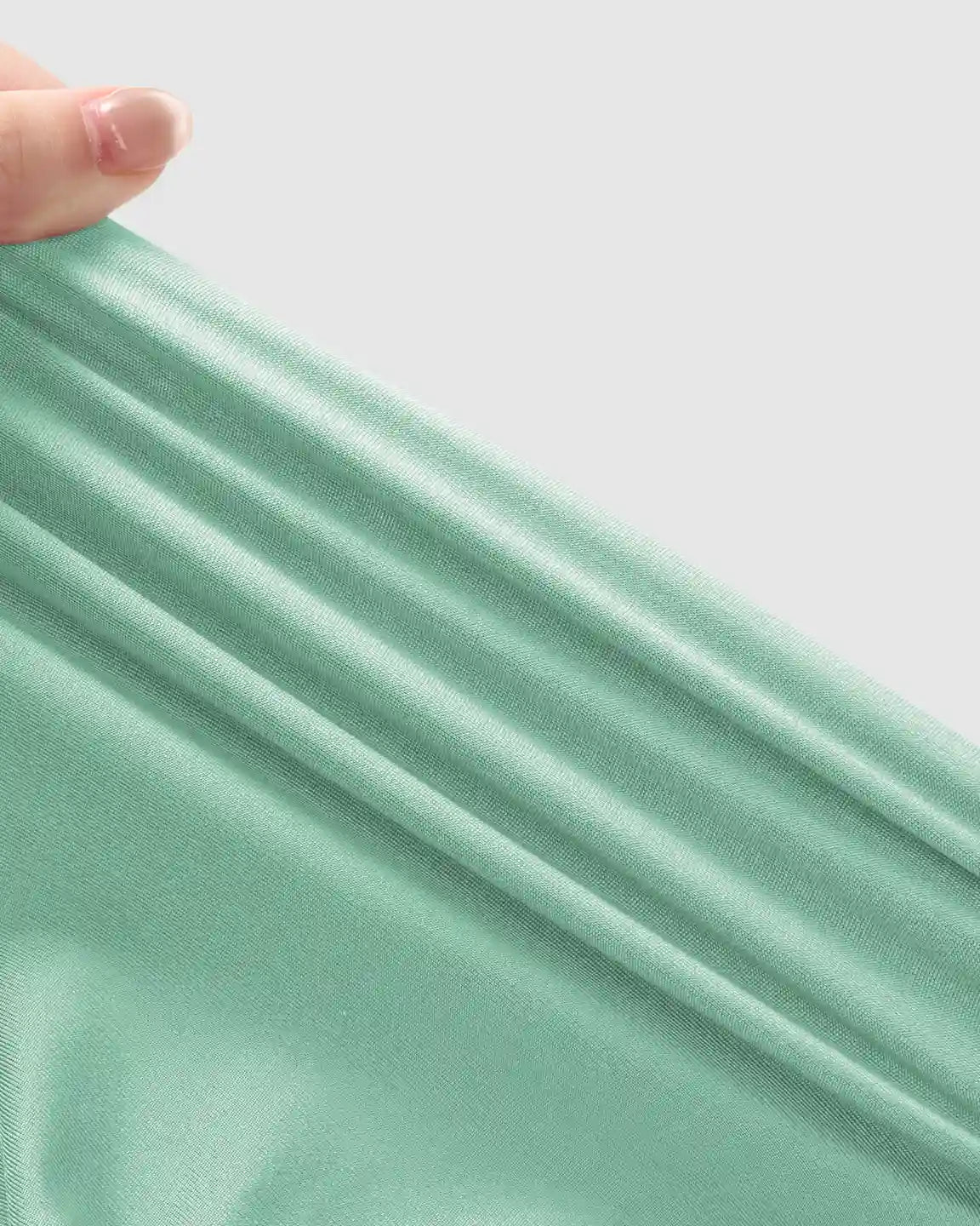Close-up of a hand stretching the soft, mint green, high-waist fabric of supportive maternity joggers.