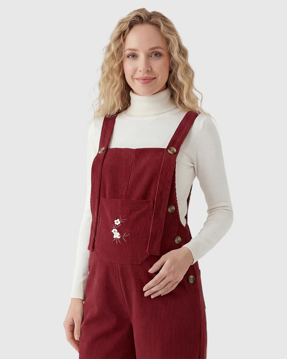 Woman in red corduroy maternity overalls with adjustable straps, front pocket, and white floral embroidery.