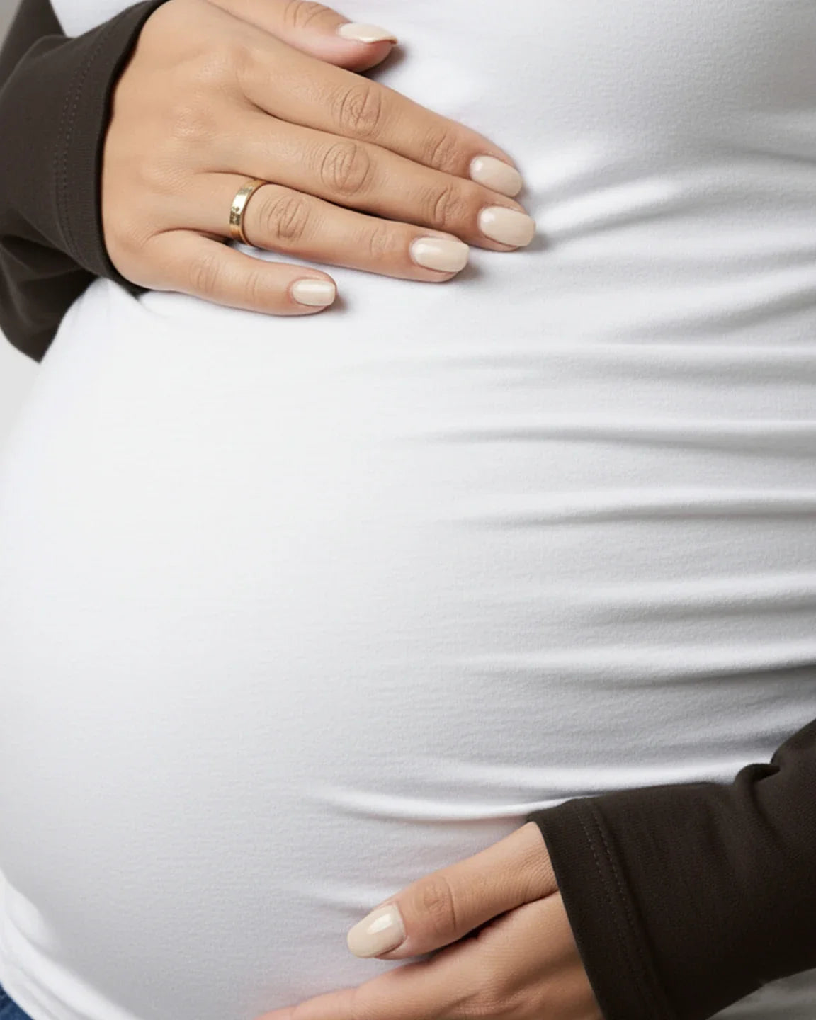 Pregnant woman in a white stretch-fit long-sleeve maternity top with dark raglan sleeves, hands on bump.
