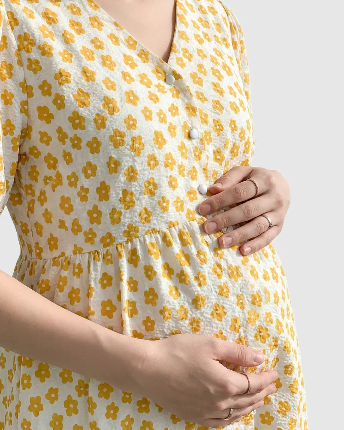 Maternity nursing dress: white with yellow floral print, V-neck, partial button-front, on a pregnant woman.