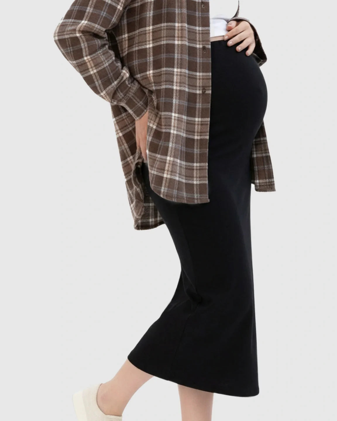 Pregnant woman in a black midi skirt and brown plaid shirt, highlighting the skirt's comfortable fit.
