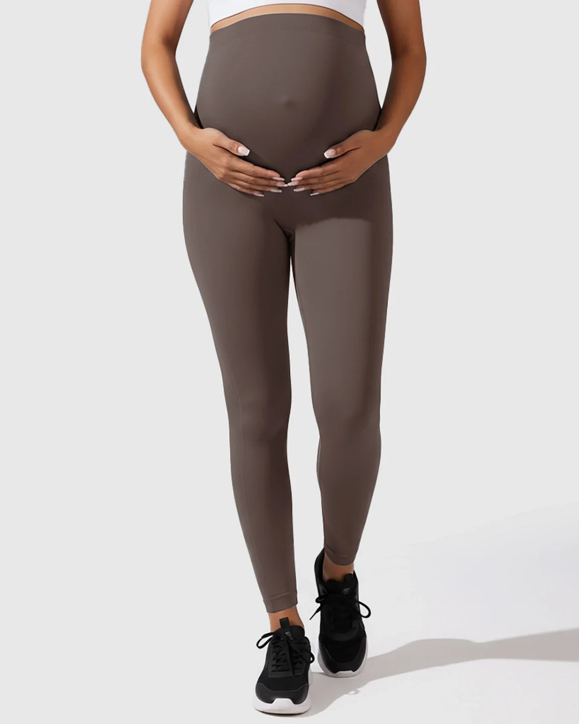 Maternity model wearing seamless, high-waisted, dark brown leggings with full-belly support.