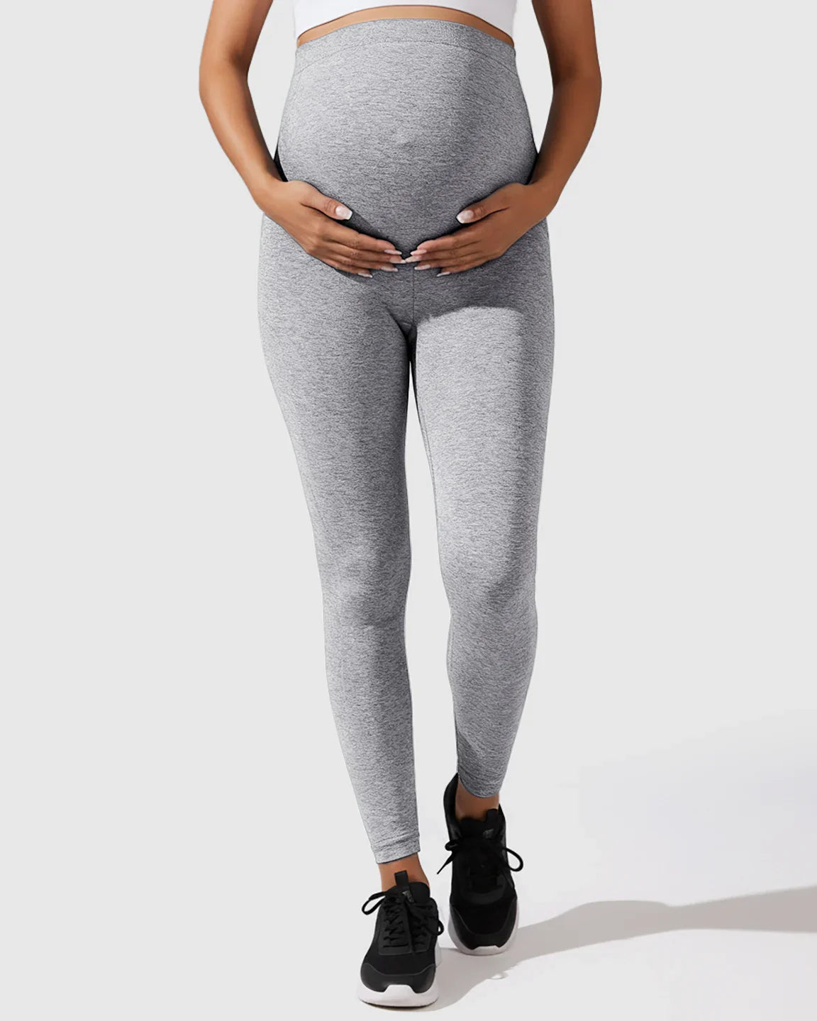 Pregnant woman wearing light gray seamless high-waisted maternity leggings, gently holding her bump.