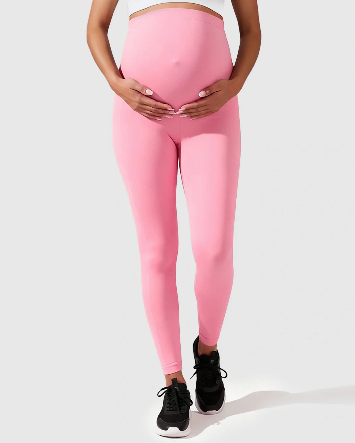 Maternity model wearing seamless pink M-shape leggings with full-belly support, gently holding her bump.