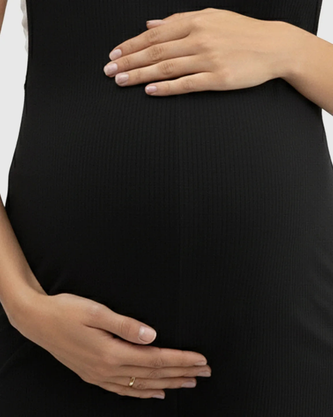 Pregnant woman wearing a black ribbed spaghetti strap wide-leg maternity jumpsuit, hands cradling her belly.