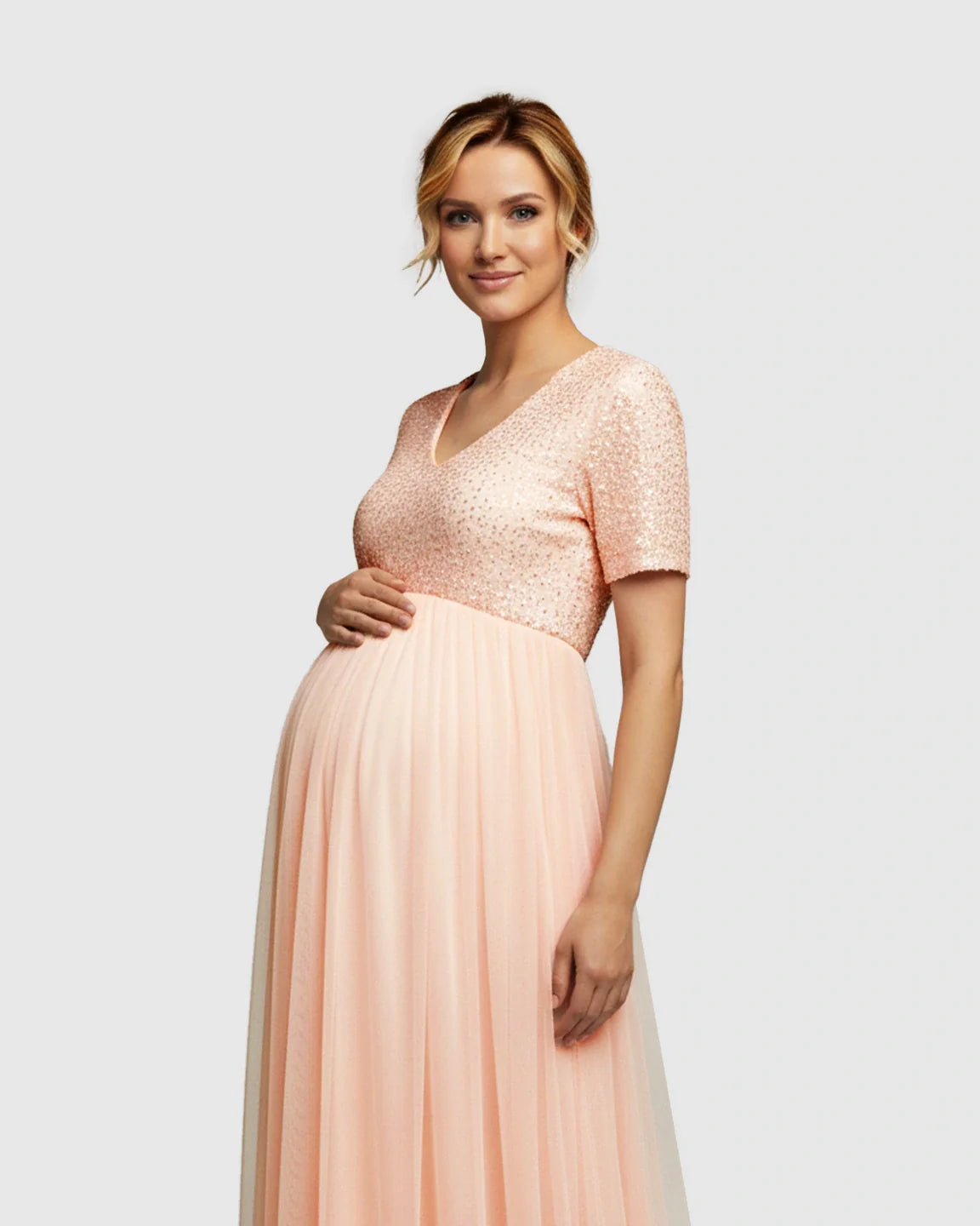 Smiling pregnant woman in a pink sequin V-neck A-line maternity evening gown with a flowing mesh skirt.