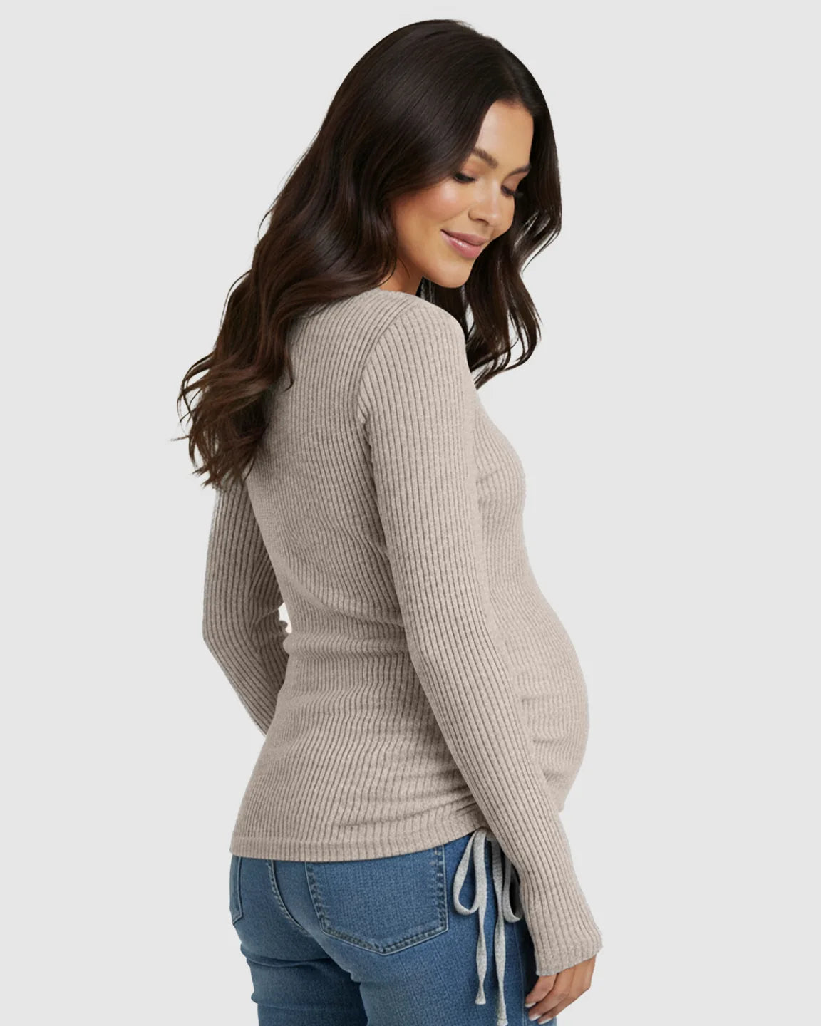 Smiling pregnant woman wearing a beige ribbed long-sleeve maternity top with adjustable side drawstrings and jeans.