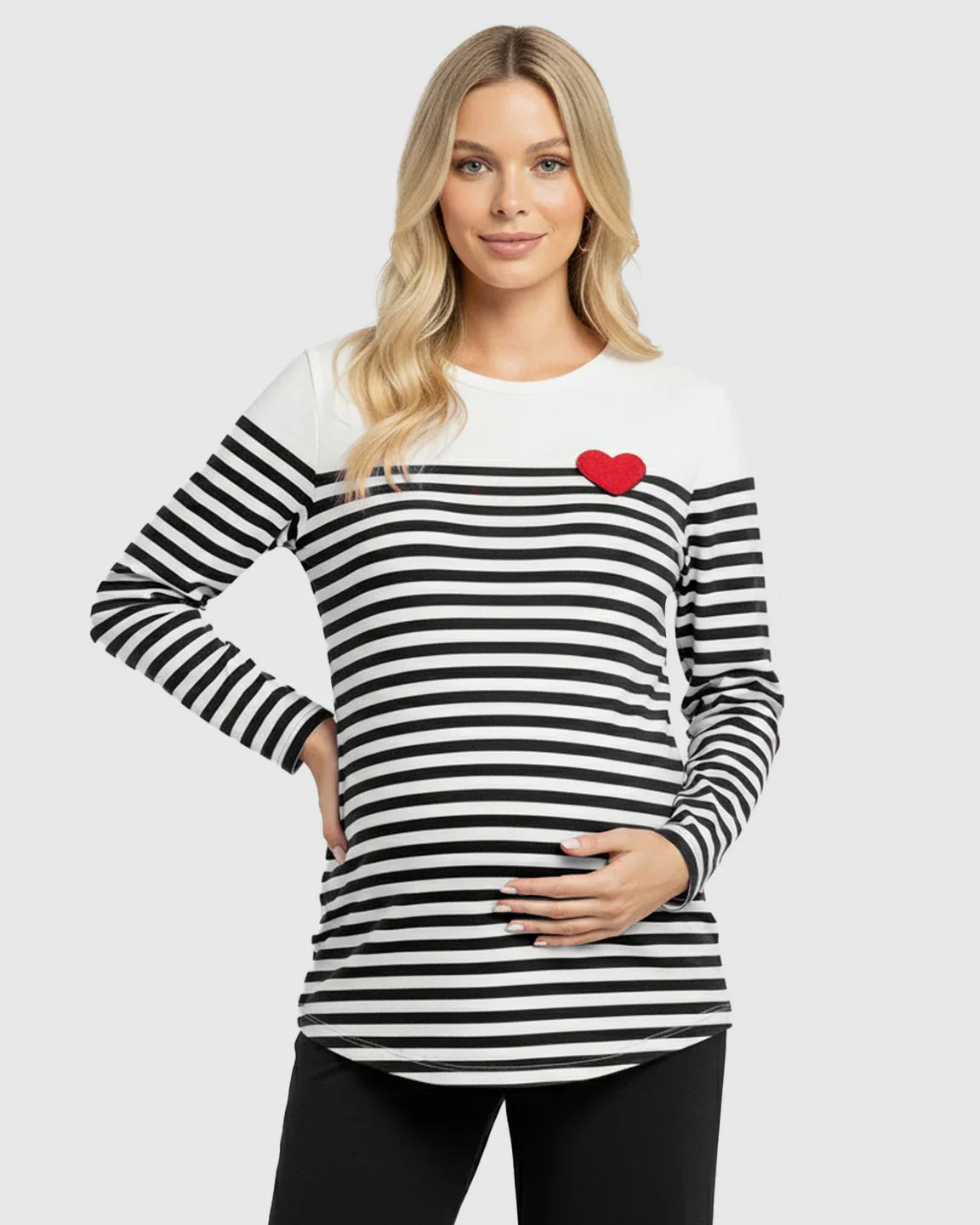 Blonde pregnant woman wearing a black and white striped long-sleeve maternity top with a red heart detail.