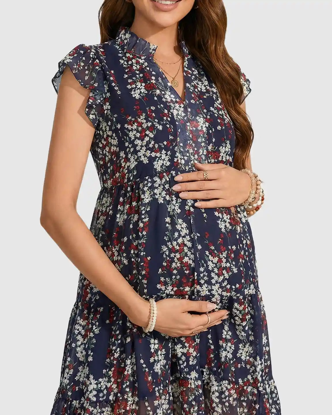 Pregnant woman in a navy floral print maternity dress with flutter sleeves and a ruffled collar, holding her bump.