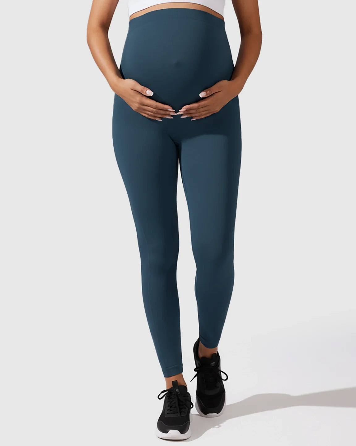 Pregnant woman modeling dark teal seamless M-shape maternity leggings with full-belly support.