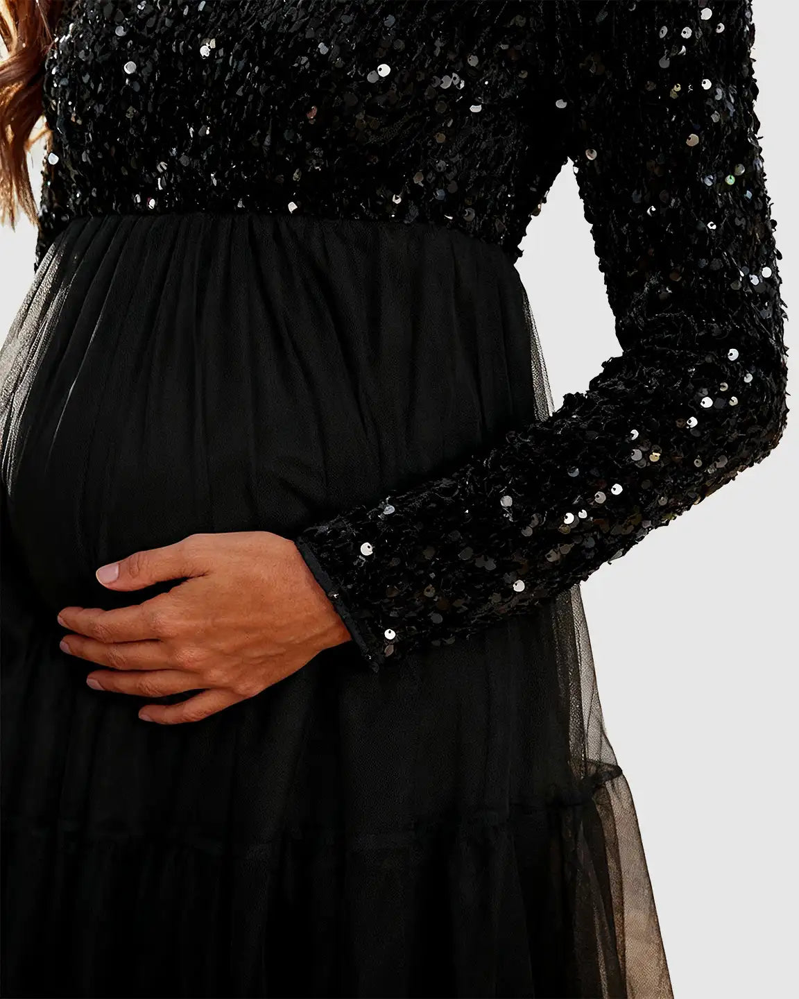 Black sequin long-sleeve empire waist maternity maxi dress with a flowing mesh skirt, worn by a pregnant woman.