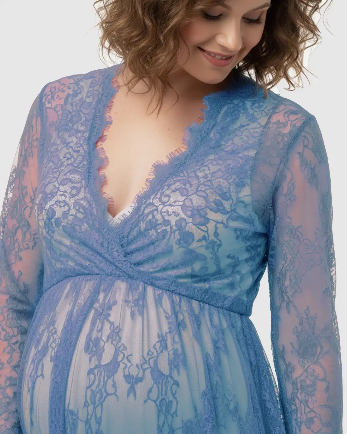 Smiling pregnant woman in a sheer floral lace empire waist maternity maxi dress in periwinkle blue.
