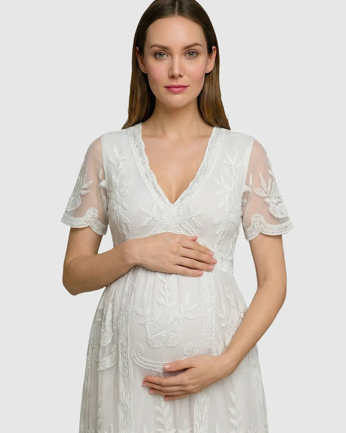 White lace maternity midi dress with V-neck, three-quarter sleeves, and floral embroidery, worn by a pregnant woman.