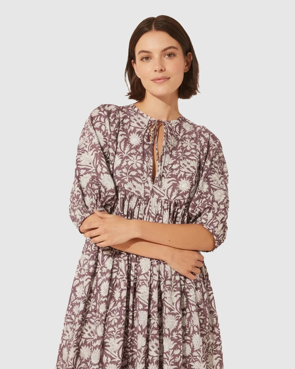Woman in a plum floral loose-fit maternity midi dress with gathered shoulders, puff sleeves, and a knot detail.