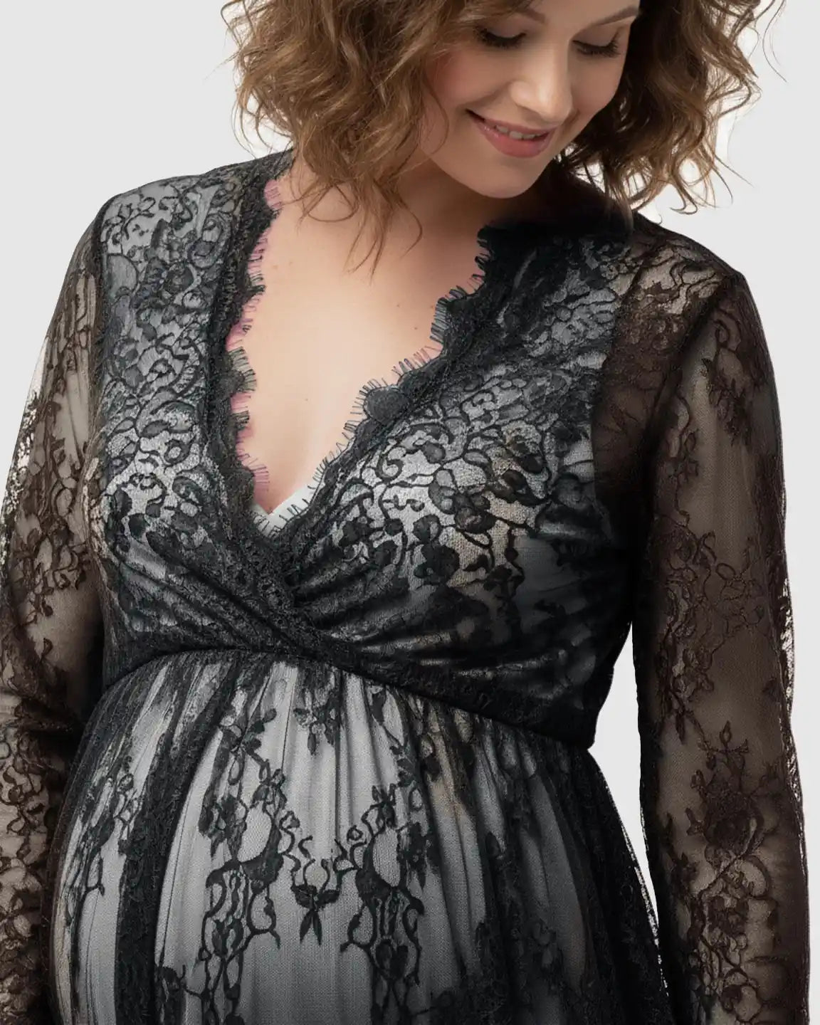 Smiling pregnant woman in a black sheer floral lace empire waist maternity maxi dress.