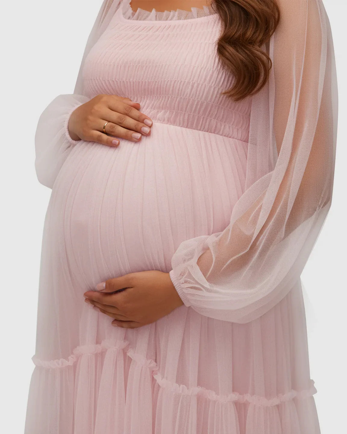 Pregnant woman in a pink tiered tulle maternity photoshoot gown with lantern sleeves, cradling her belly.
