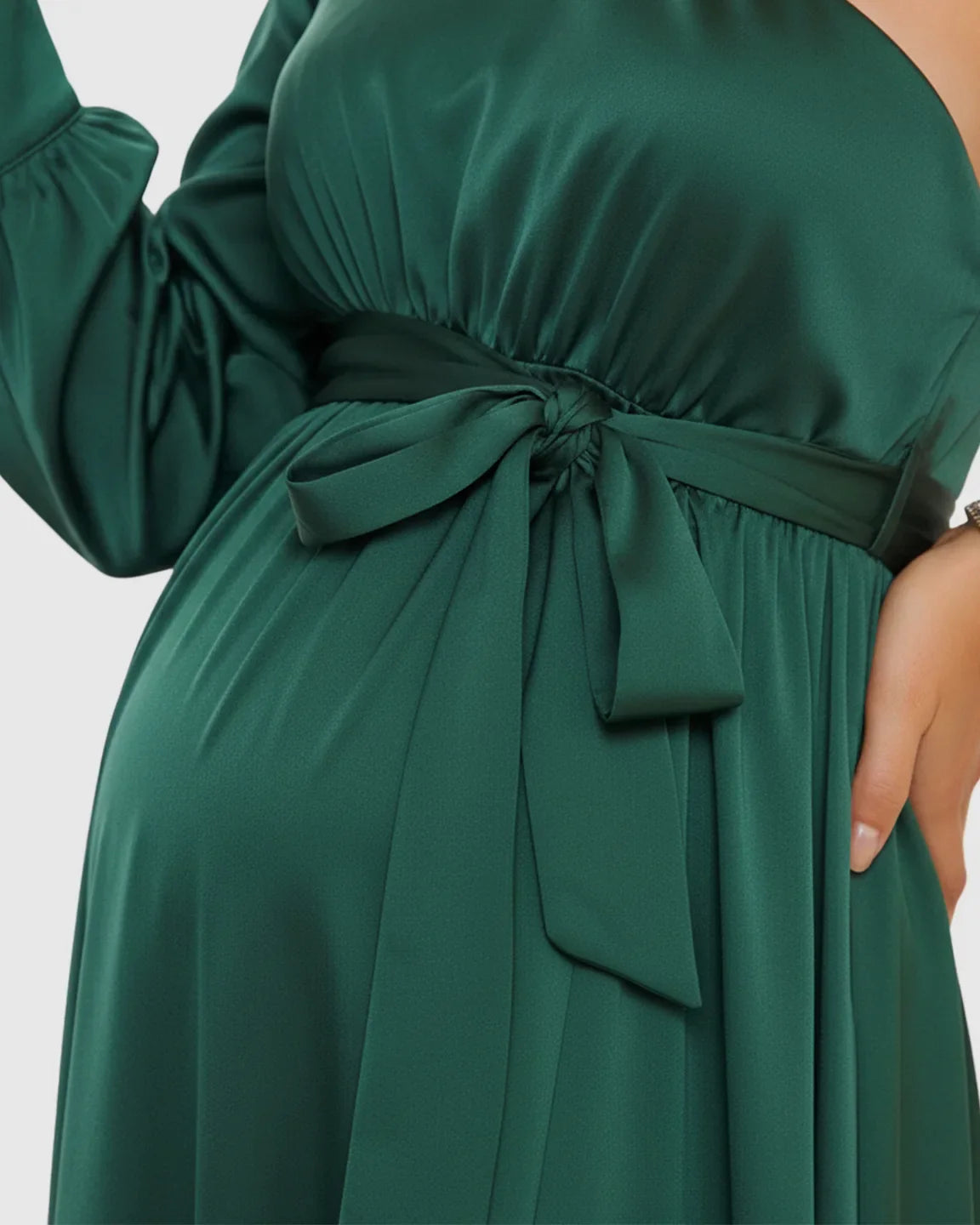 Elegant emerald green satin one-shoulder maternity maxi dress with a tie-waist detail highlighting the bump.