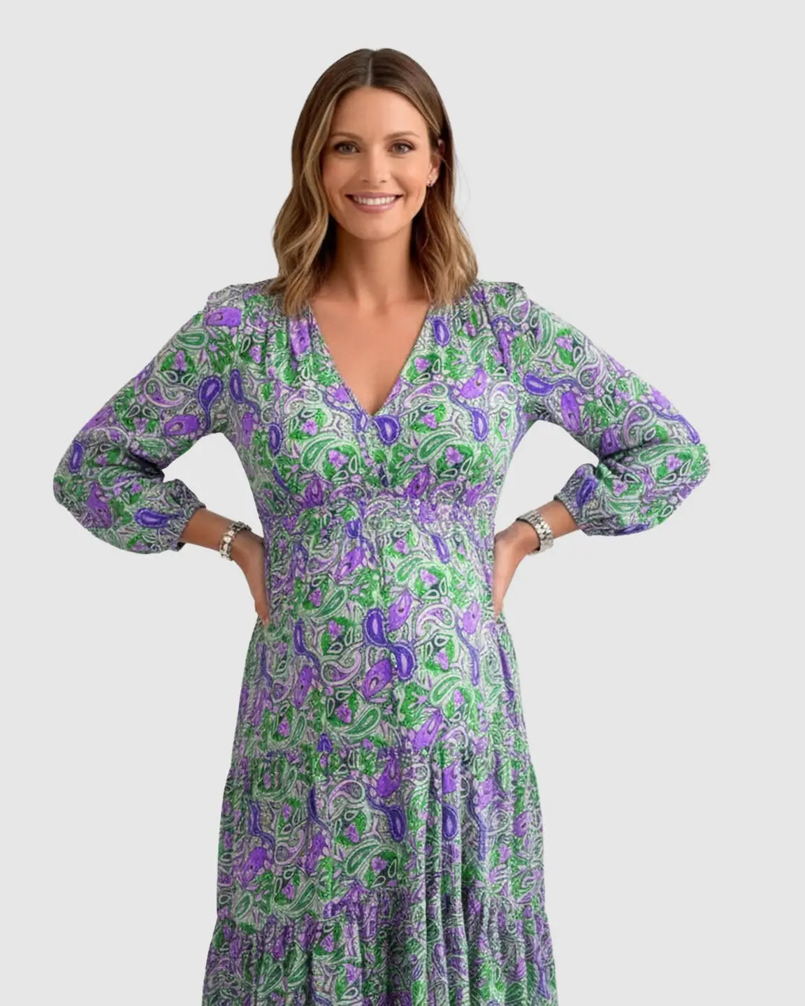 Smiling pregnant woman in a green and purple paisley flowy maxi dress with a V-neck and tie waist.