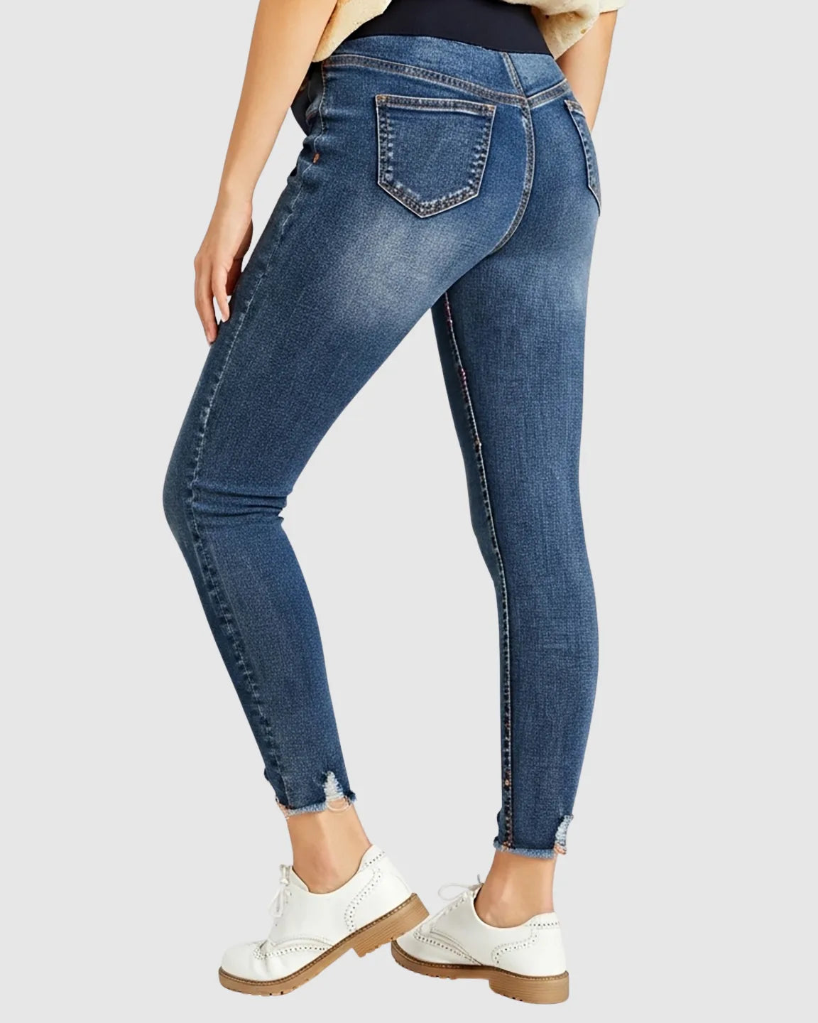 Woman wearing dark wash distressed skinny maternity jeans with frayed hems and a high-rise elastic waistband.