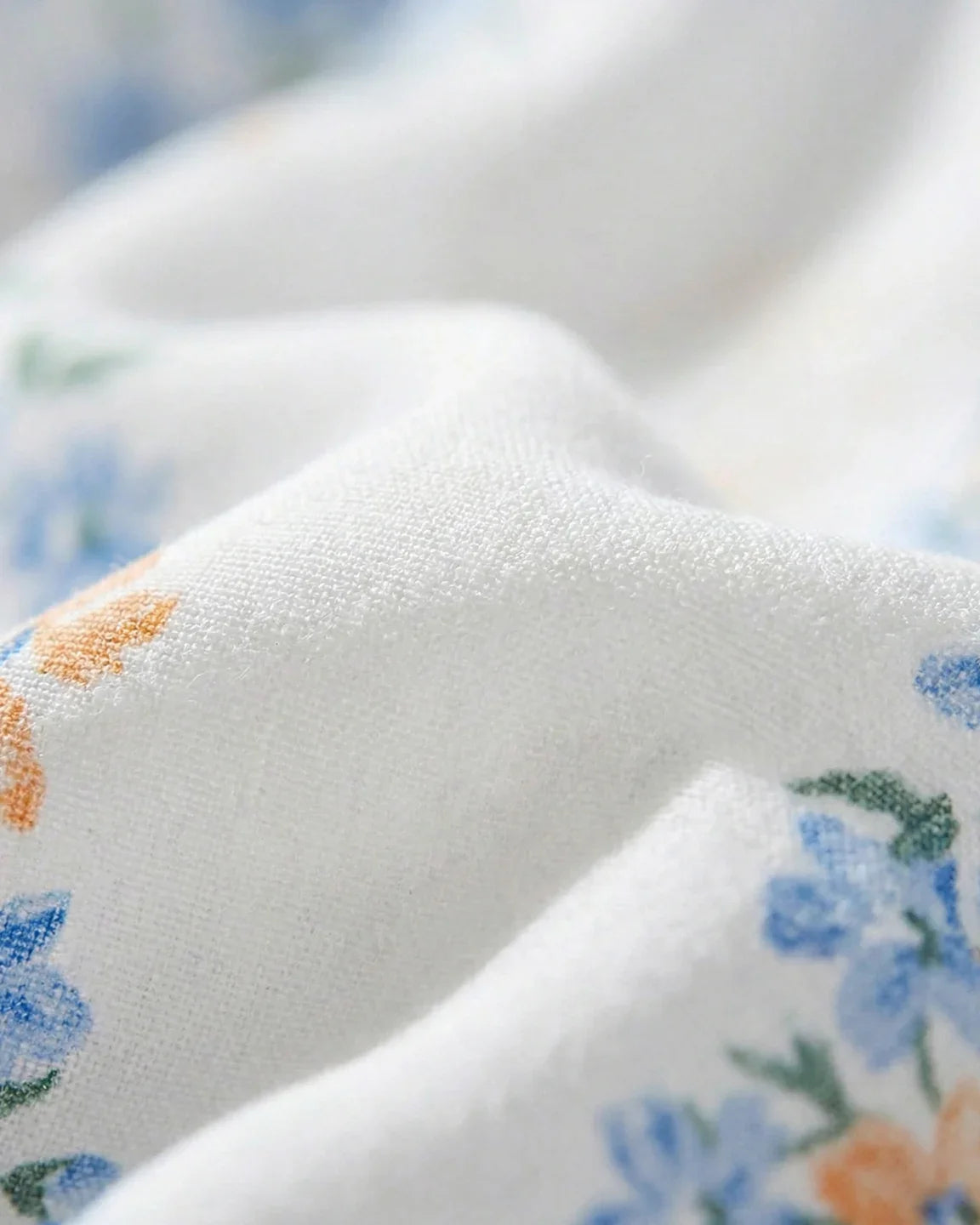 Close-up of white chiffon maternity dress fabric with blue and orange floral print.
