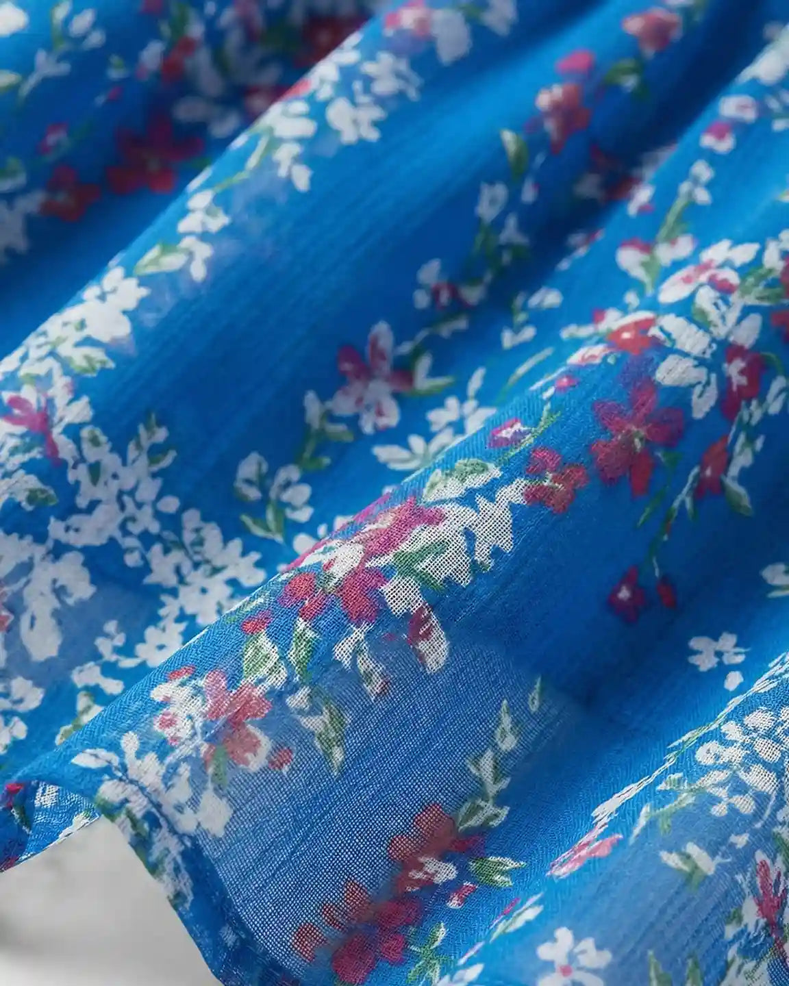 Close-up of a blue chiffon maternity dress with a soft floral print in white and red.