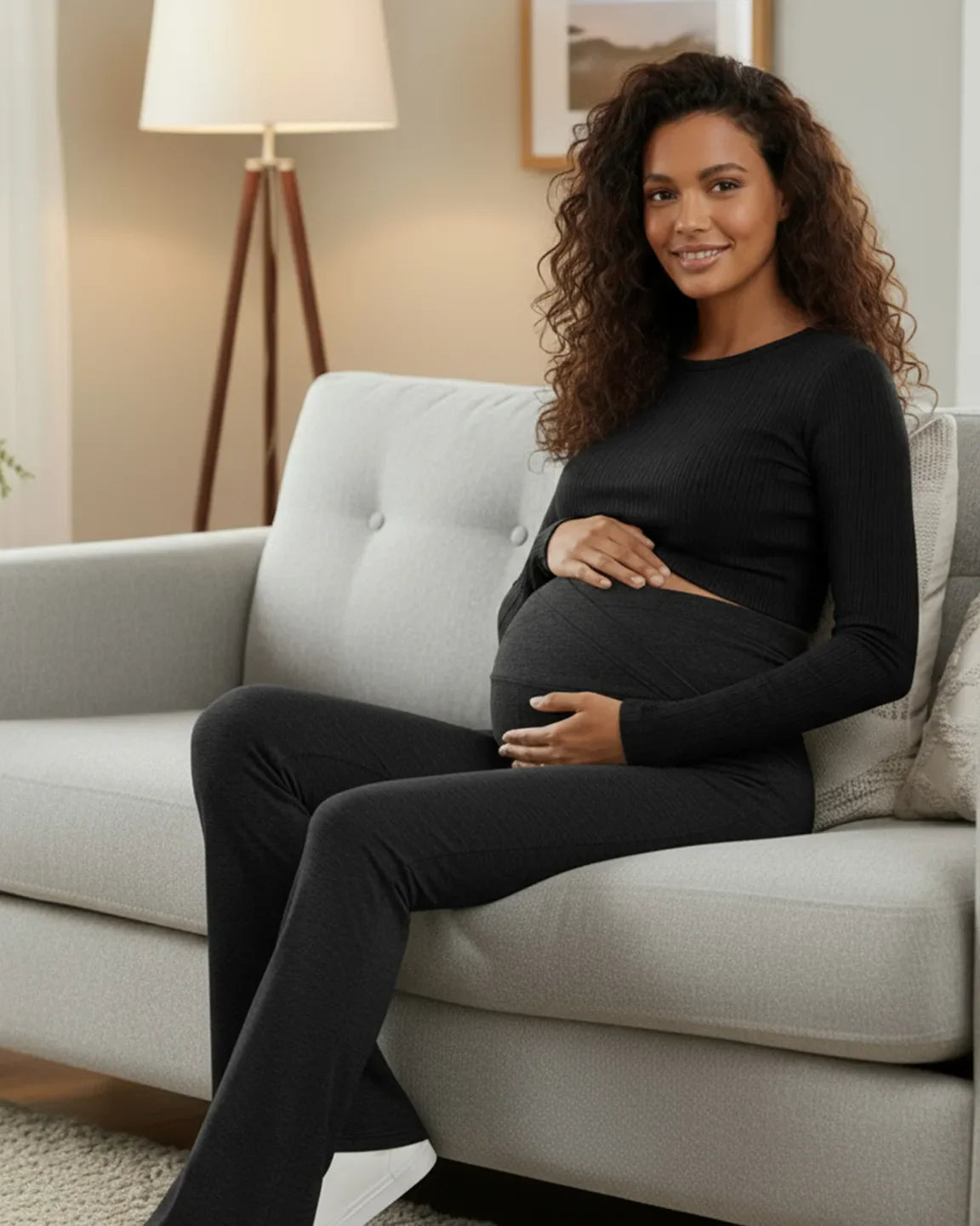 Smiling pregnant woman in black ribbed top and dark gray crossed waistband flared maternity pants.