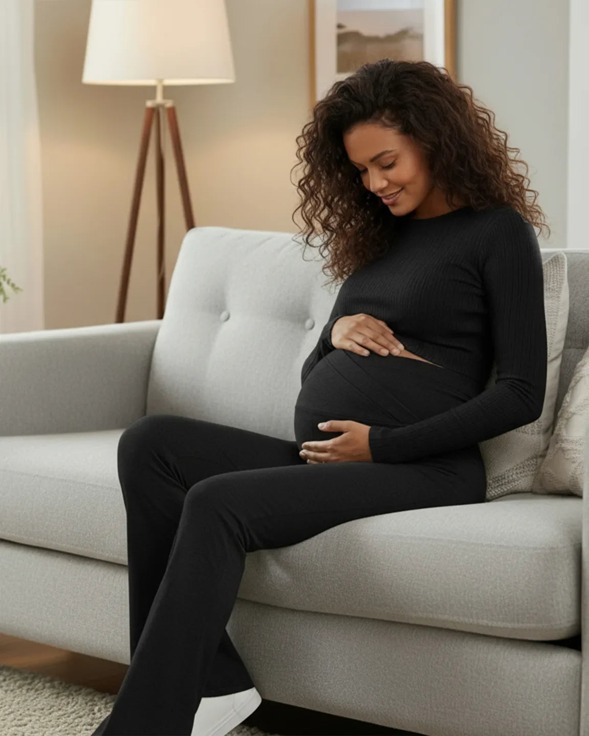 Smiling pregnant woman in black ribbed long-sleeve top and Bump Society crossed waistband flared maternity pants.