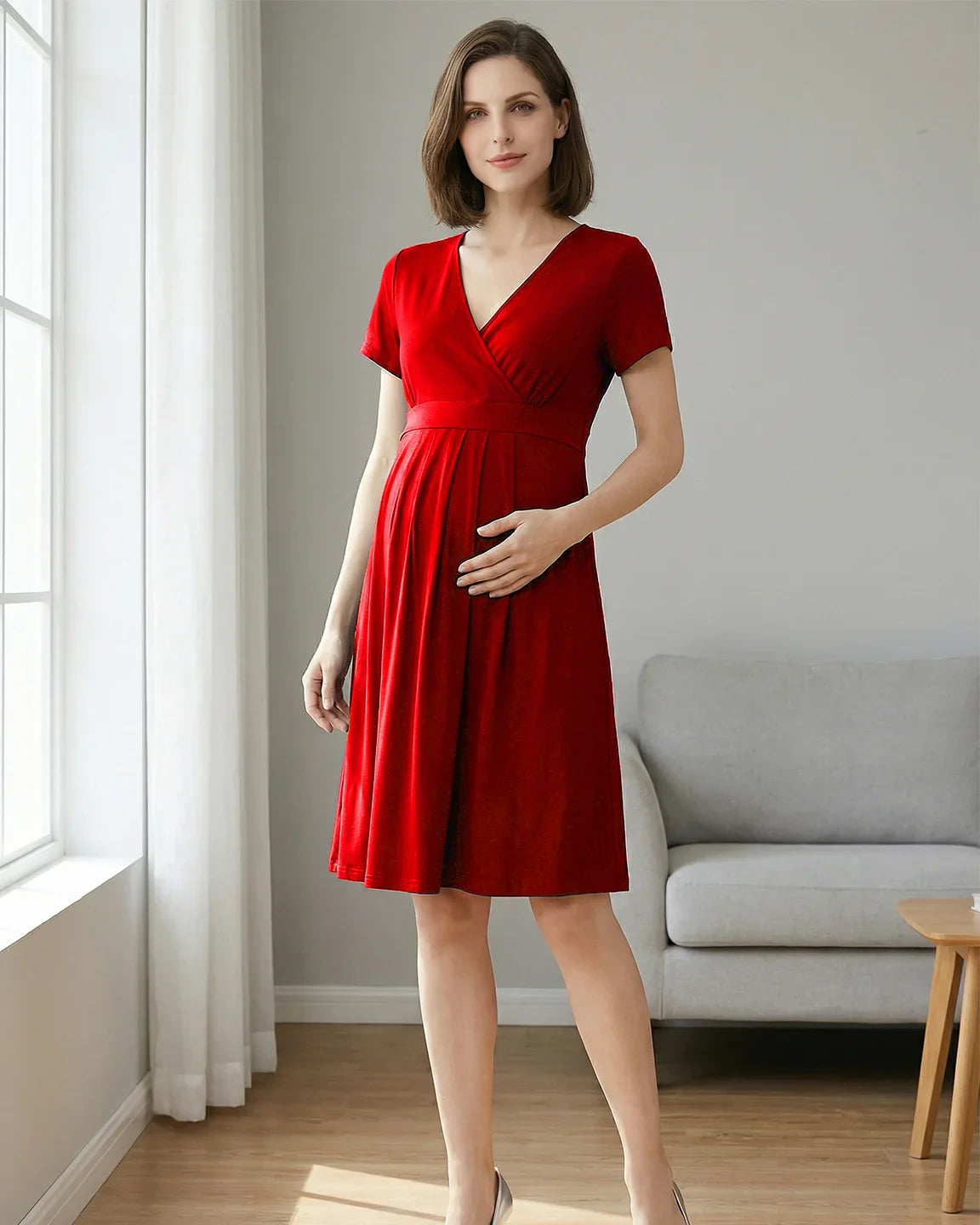 Woman in a red V-neck A-line maternity and nursing dress with short sleeves, holding her bump.