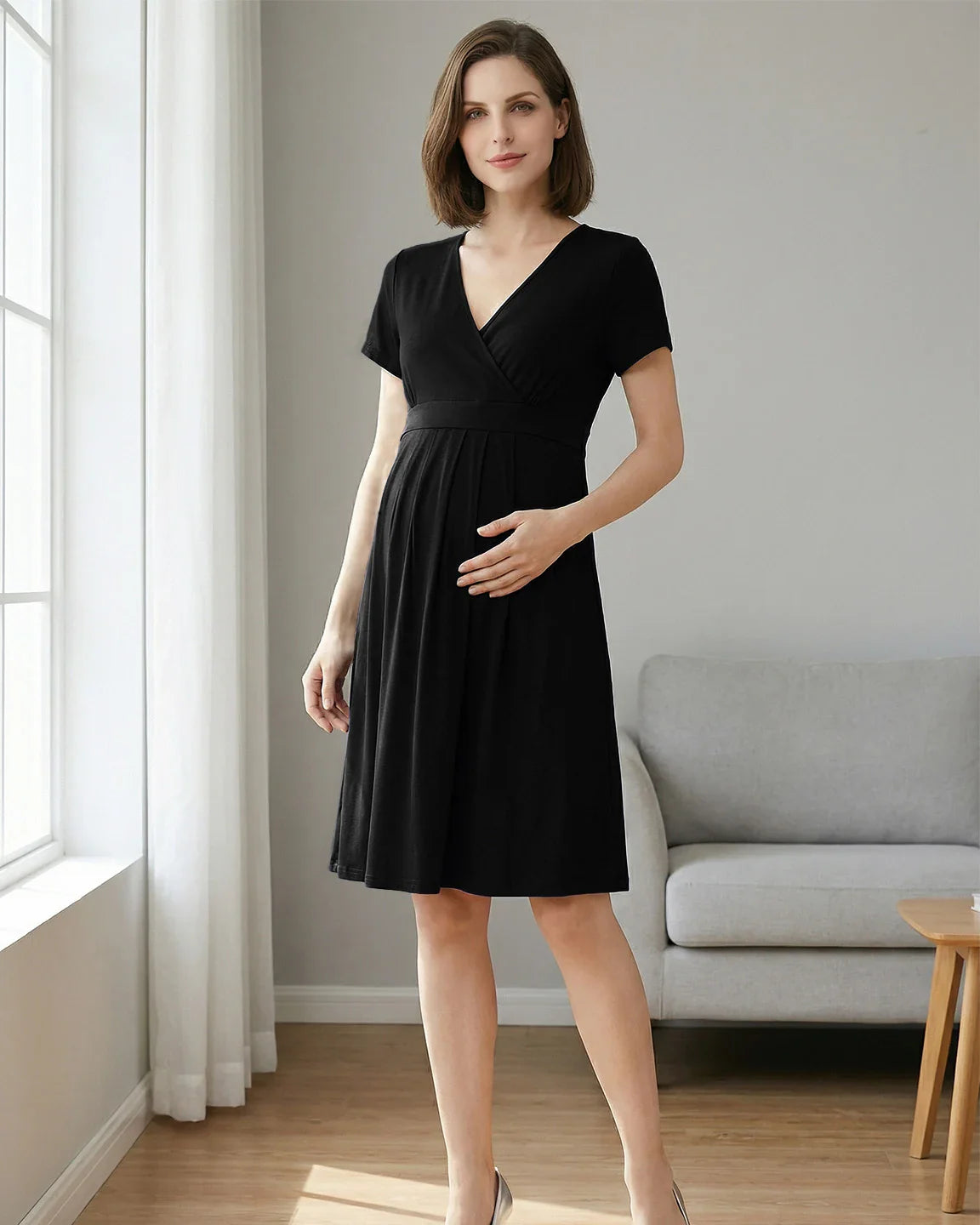 Woman in a black V-neck A-line maternity and nursing dress with short sleeves, holding her baby bump.