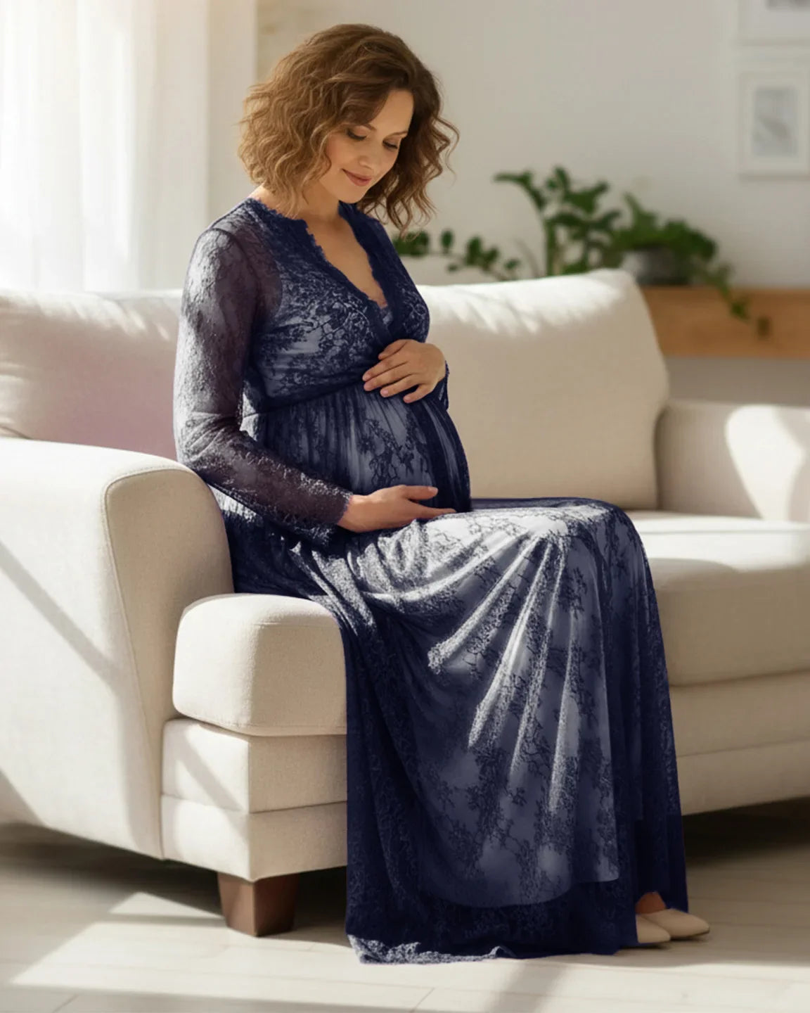 Pregnant woman in a navy sheer floral lace empire waist maternity maxi dress, gently holding her bump.
