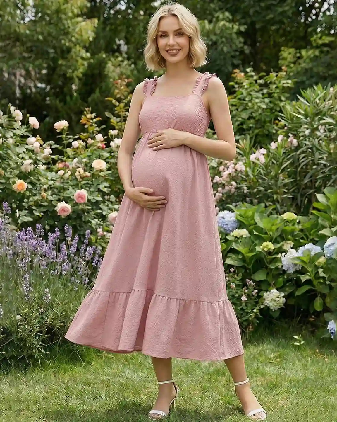 Pregnant woman in a pink ruffled strap maternity maxi dress with a tiered skirt, standing in a garden.