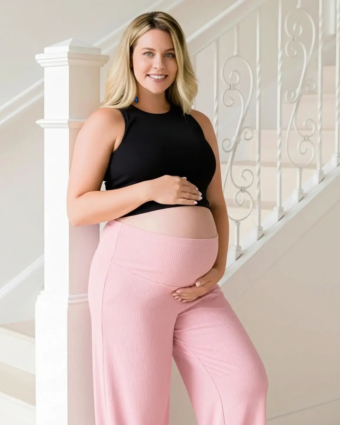 Smiling pregnant woman in pink ribbed wide-leg maternity pants with an over-bump waistband.