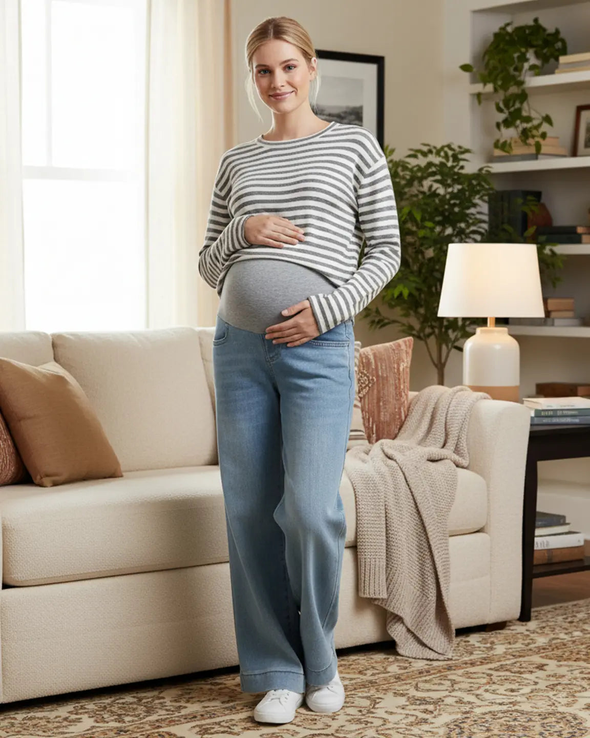 Smiling pregnant woman in light wash wide leg maternity jeans with a folded hem and gray belly band.
