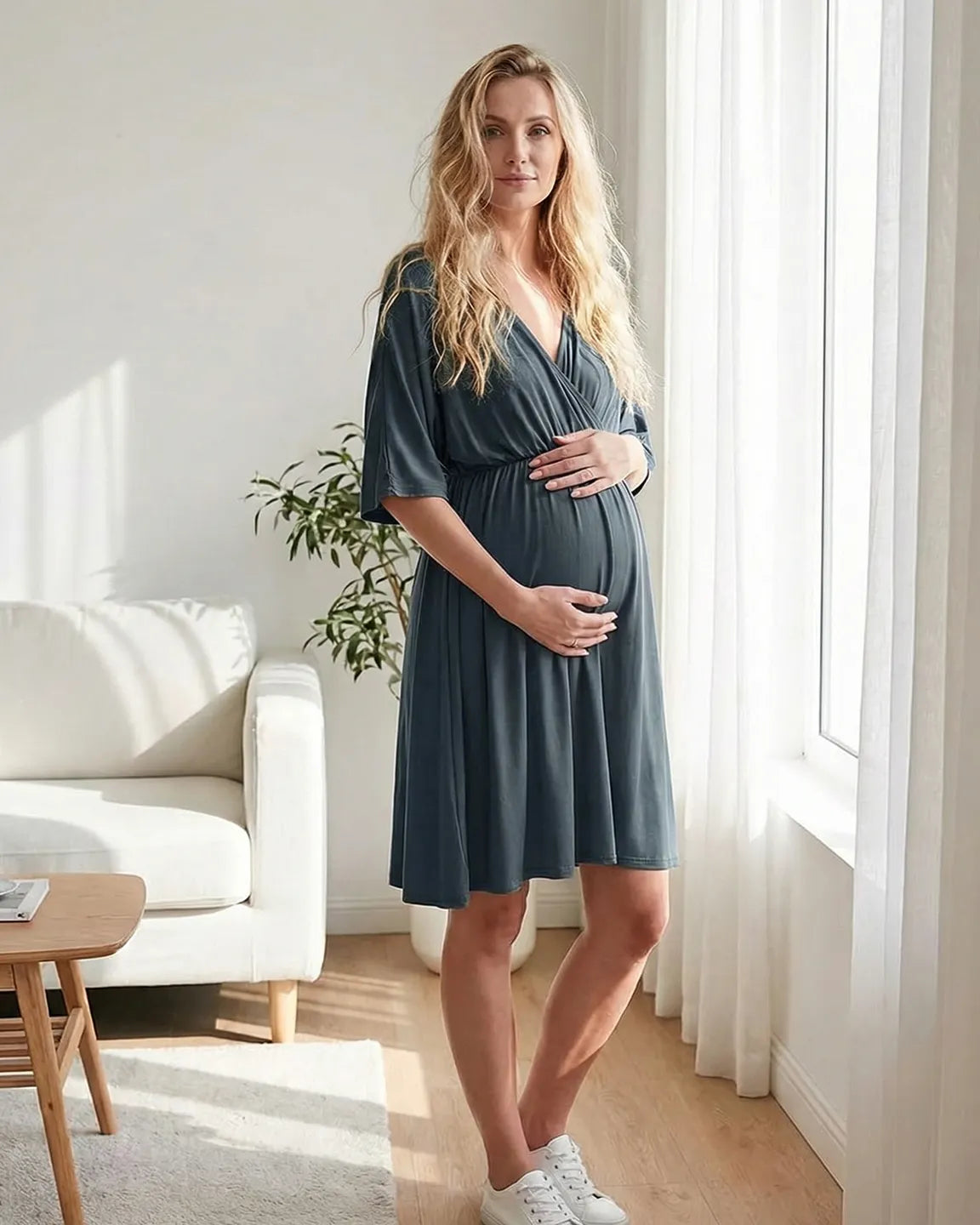 Pregnant woman in a slate blue cross-front maternity midi dress with 3/4 sleeves, holding her bump.