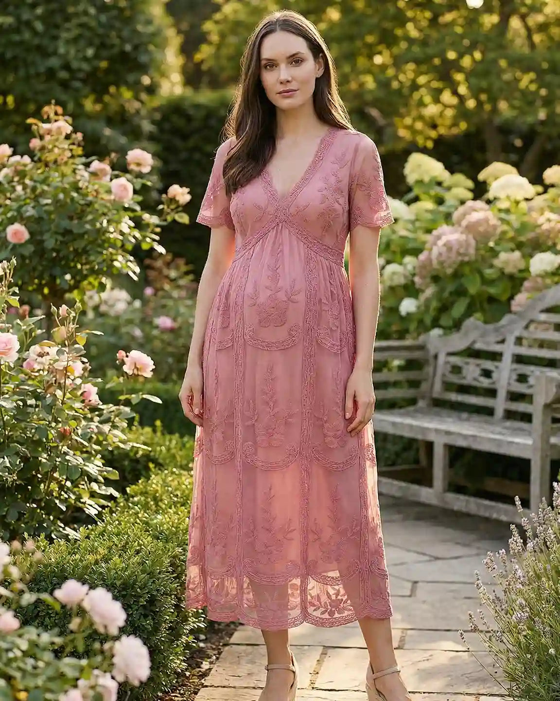 Maternity midi dress in dusty rose lace with V-neck, three-quarter sleeves, and swing skirt, worn in a garden.