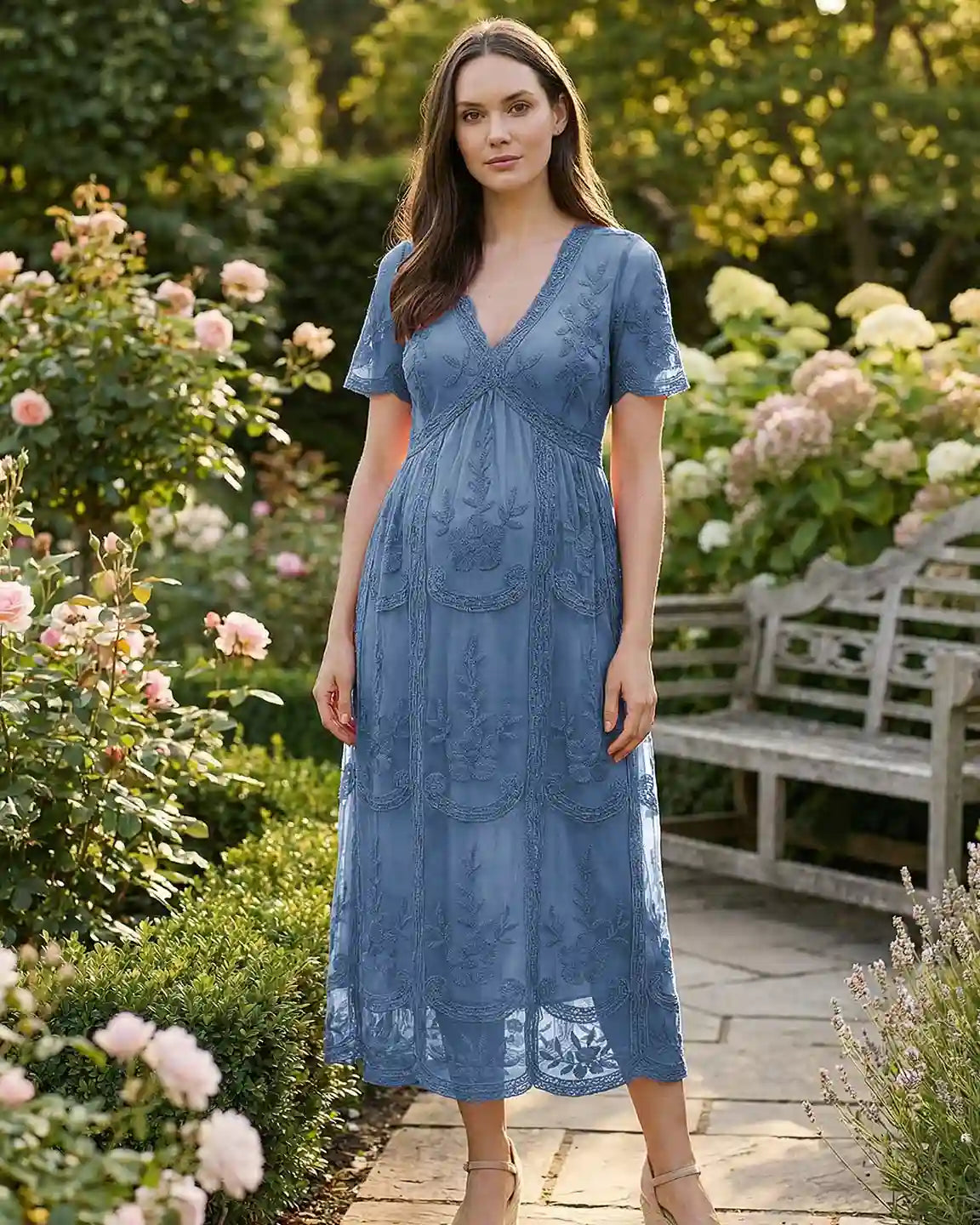 Maternity midi dress in dusty blue lace with V-neck, three-quarter sleeves, and swing skirt, worn in a garden.