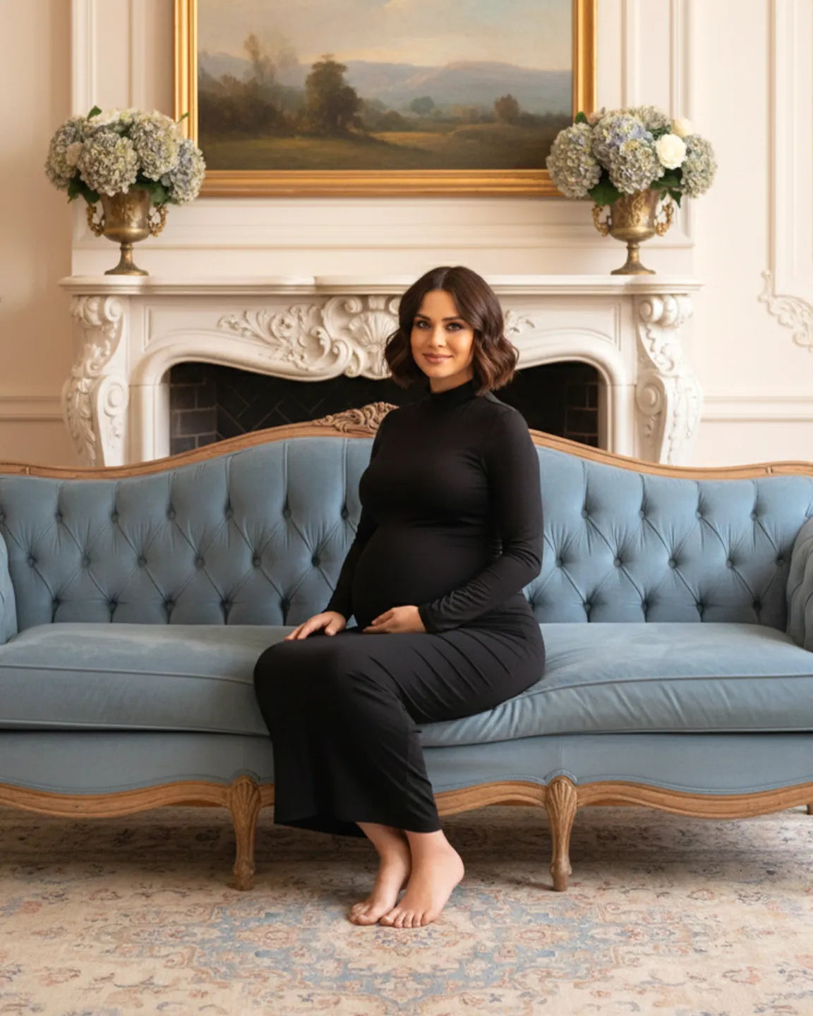 Pregnant woman in a black long-sleeve mock-neck bodycon maternity maxi dress sitting on a blue sofa.
