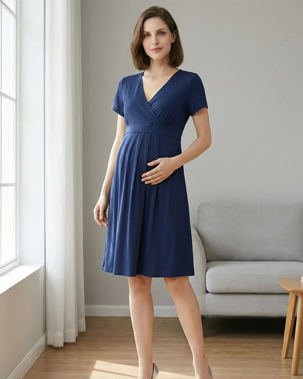 Woman in a navy V-neck A-line maternity and nursing dress with short sleeves, holding her bump.