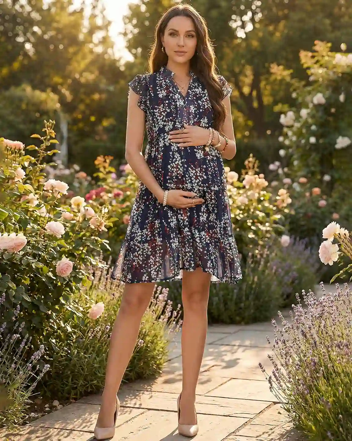 Pregnant woman in a navy floral print chiffon maternity dress with flutter sleeves, standing in a rose garden.
