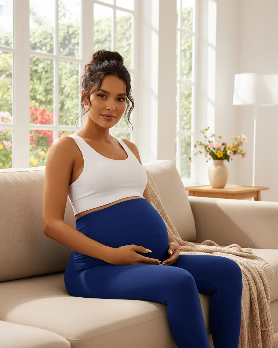 Pregnant woman in white crop top and royal blue seamless M-shape maternity leggings, sitting on a sofa.