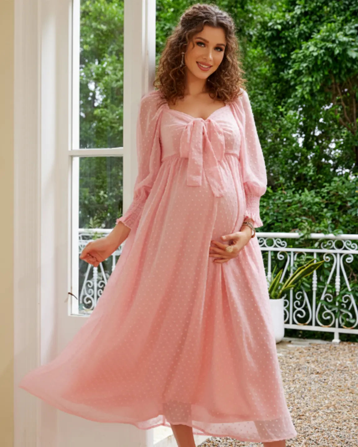 Pregnant woman in a pink polka-dot chiffon maternity maxi dress with a square neckline and long sleeves.