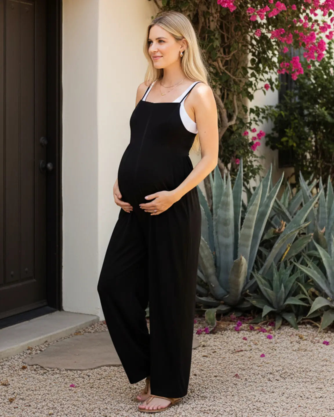 Pregnant woman in a black spaghetti strap wide-leg maternity jumpsuit with a white top underneath.