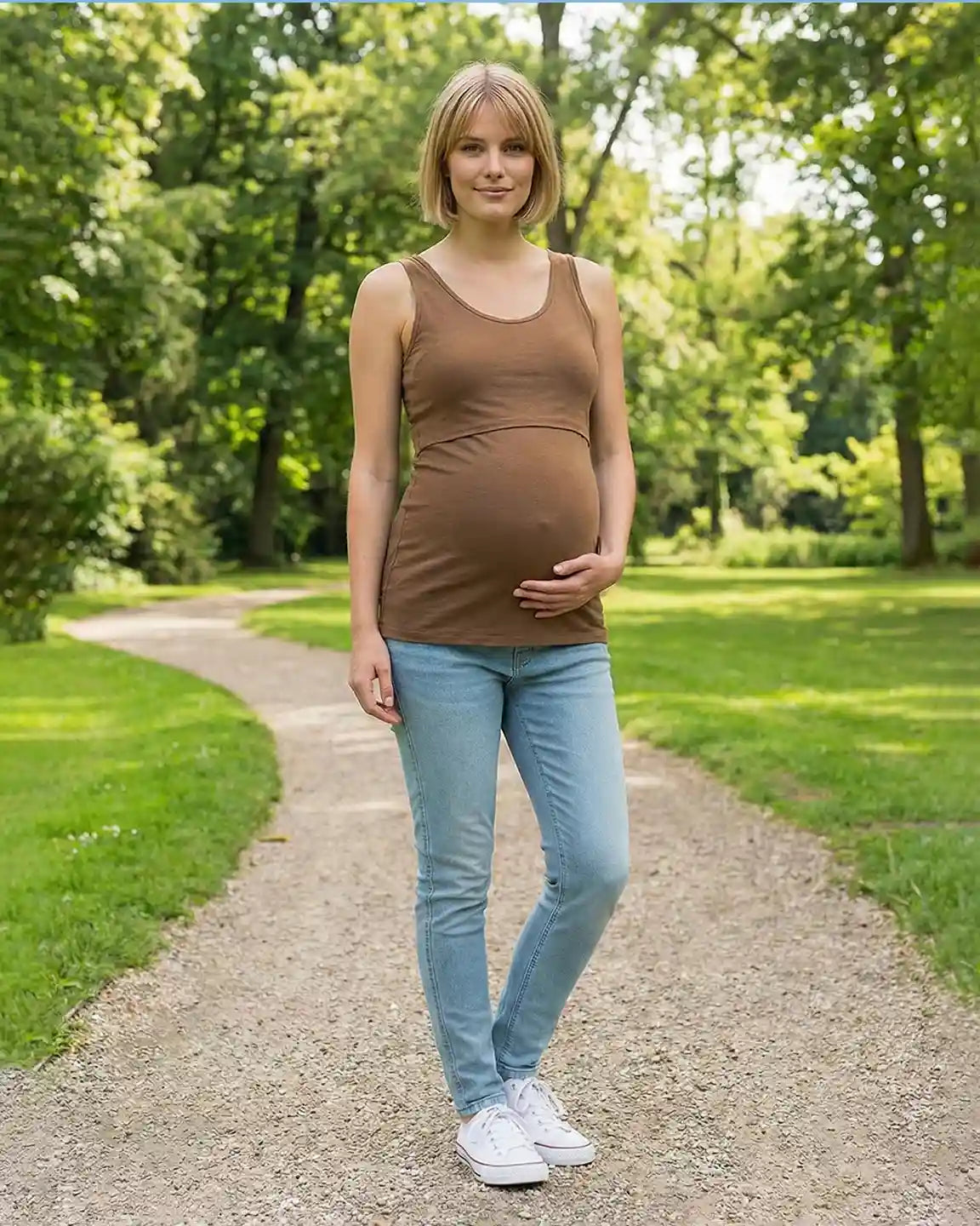 Pregnant woman in a brown stretch nursing-access maternity tank top and jeans, holding her belly.