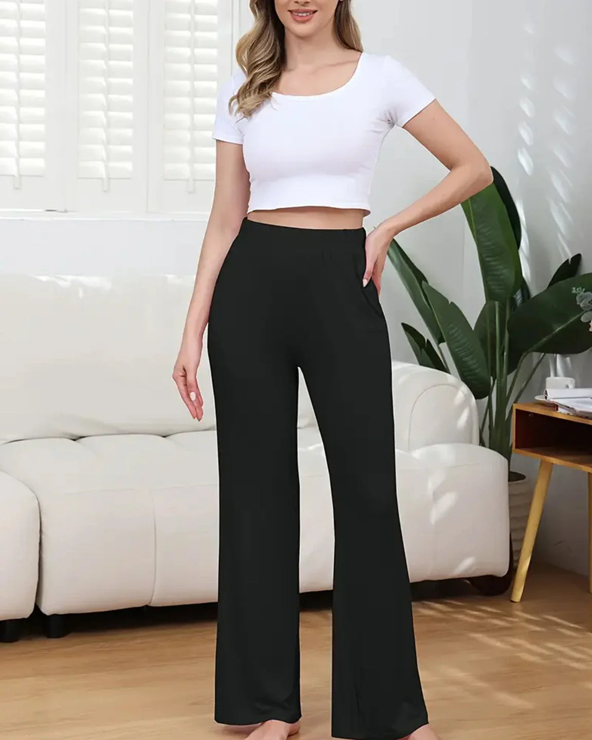 Woman wearing black stretch flared maternity pants with pockets and a white crop top.
