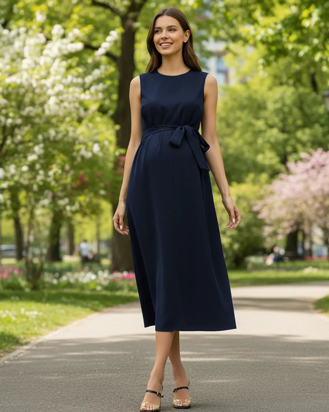 Smiling pregnant woman in a navy tie-waist V-neck maternity midi dress, walking outdoors.