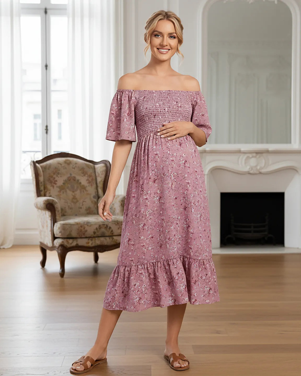 Smiling pregnant woman in a pink floral off-shoulder smocked maternity midi dress with flutter sleeves.