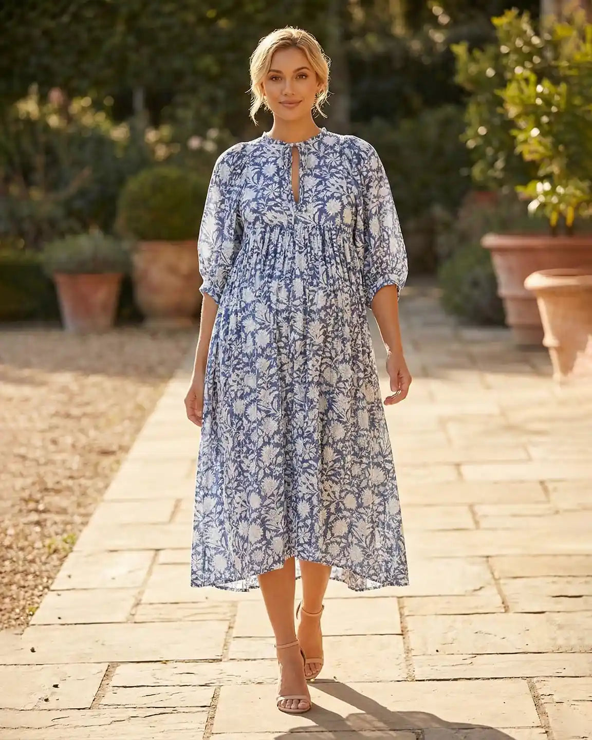 Woman in blue and white floral maternity midi dress with gathered shoulders, puff sleeves, and knot detail.