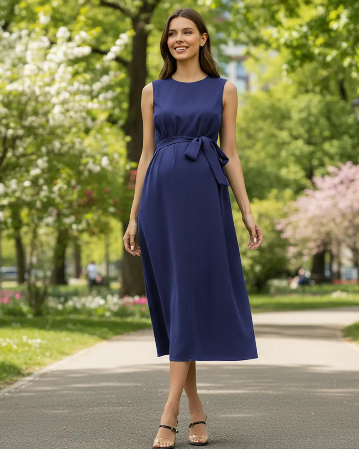 Smiling pregnant woman in a navy blue tie-waist maternity midi dress with a round neck, walking outdoors.